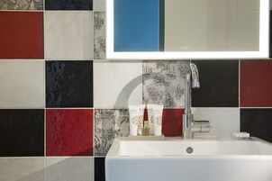 Een badkamer met een wit wastafeltje, een spiegel erboven en een betegelde muur met een combinatie van rode, zwarte en witte tegels.