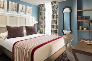 A hotel room with a large bed, a desk, a chair, and a bookshelf.