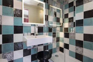 Un baño con salpicadero de azulejos a cuadros, un lavamanos blanco, un inodoro negro y un espejo sobre el lavamanos.
