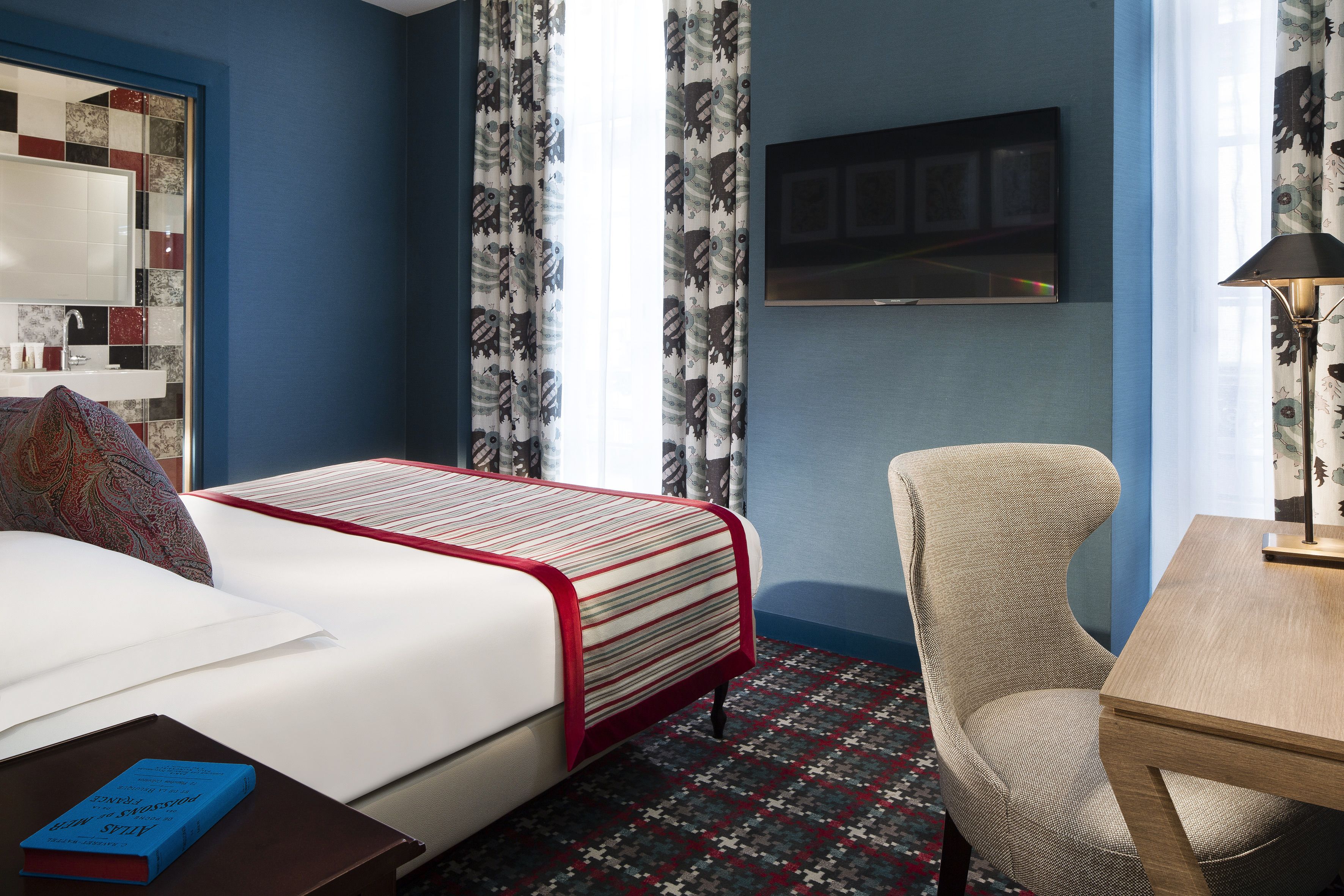 Una habitación de hotel con cama, una silla, una mesa, un televisor y una alfombra estampada.