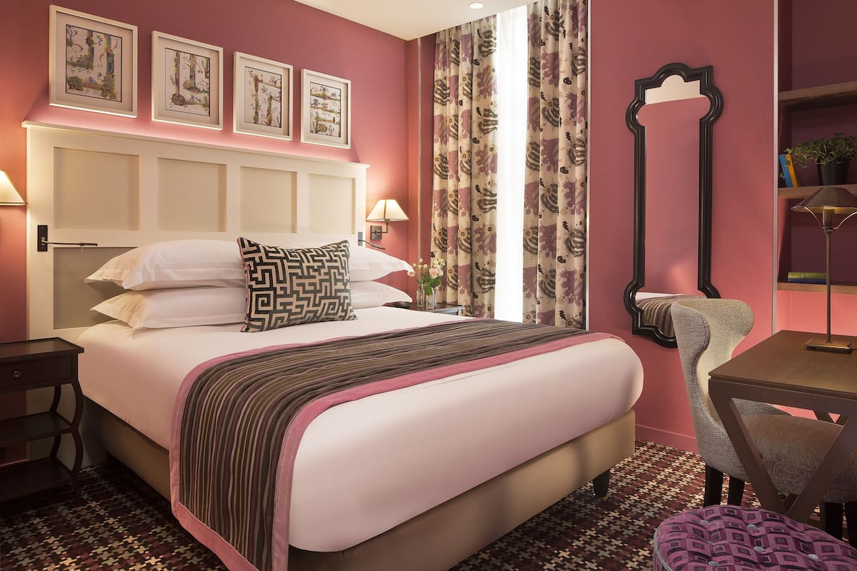 A neatly made bed with a striped blanket, a headboard with a decorative panel, and a bedside table with a lamp.