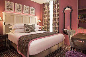 Quarto de hotel com uma cama grande, uma escrivaninha, uma cadeira e um espelho.