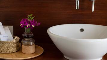 A white basin sink on a wooden countertop with a woven basket and a small jar.