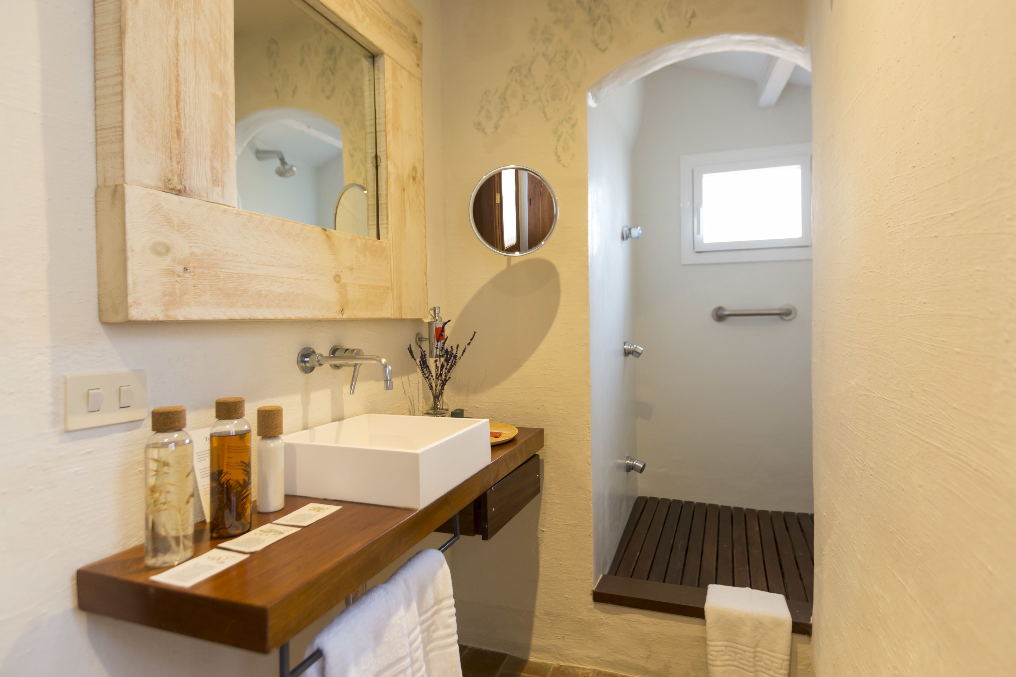 Une salle de bain avec un meuble-lavabo en bois, un grand miroir, un lavabo blanc et un espace douche.