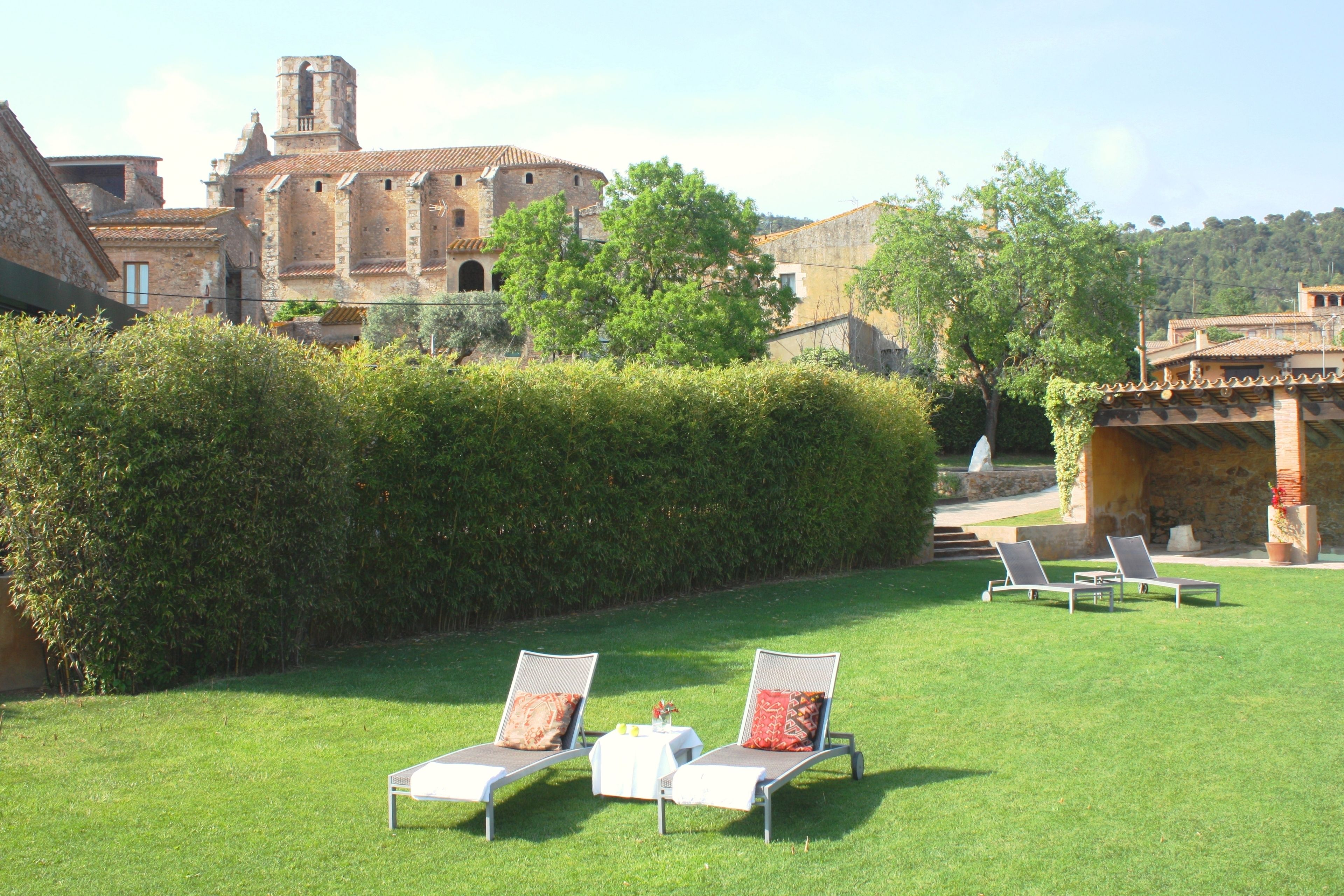 Un patio con dos sillones, una mesa con un florero y un edificio histórico al fondo.
