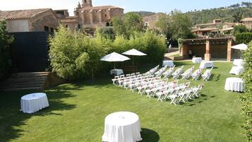 An outdoor wedding venue with white tables and chairs, surrounded by greenery and historic buildings in the background.