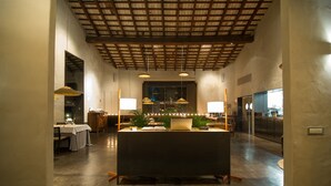 Un hall d’hôtel spacieux avec un comptoir d’accueil central, un grand espace de restauration et une cuisine visible à travers une paroi en verre.