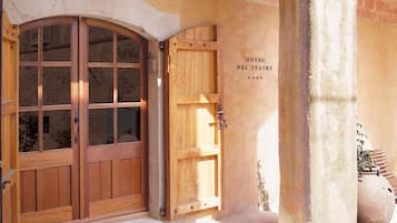 Eine Holztür mit Doppelverriegelung und Glasfenster, eine kleinere Holztür und eine Steinmauer mit der Aufschrift „HOTEL DEL TEATRE“.