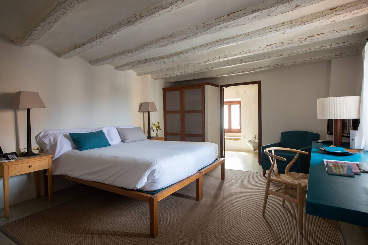 Une chambre à coucher avec un lit en bois, deux tables de chevet avec des lampes, un bureau avec une chaise et une vue sur l’extérieur.