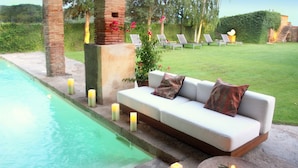 Un espace aménagé au bord de la piscine, avec un canapé blanc, des bougies et des chaises longues.