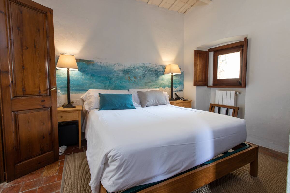 Une chambre à coucher avec un lit en bois, deux tables de chevet avec des lampes, une fenêtre et une porte.