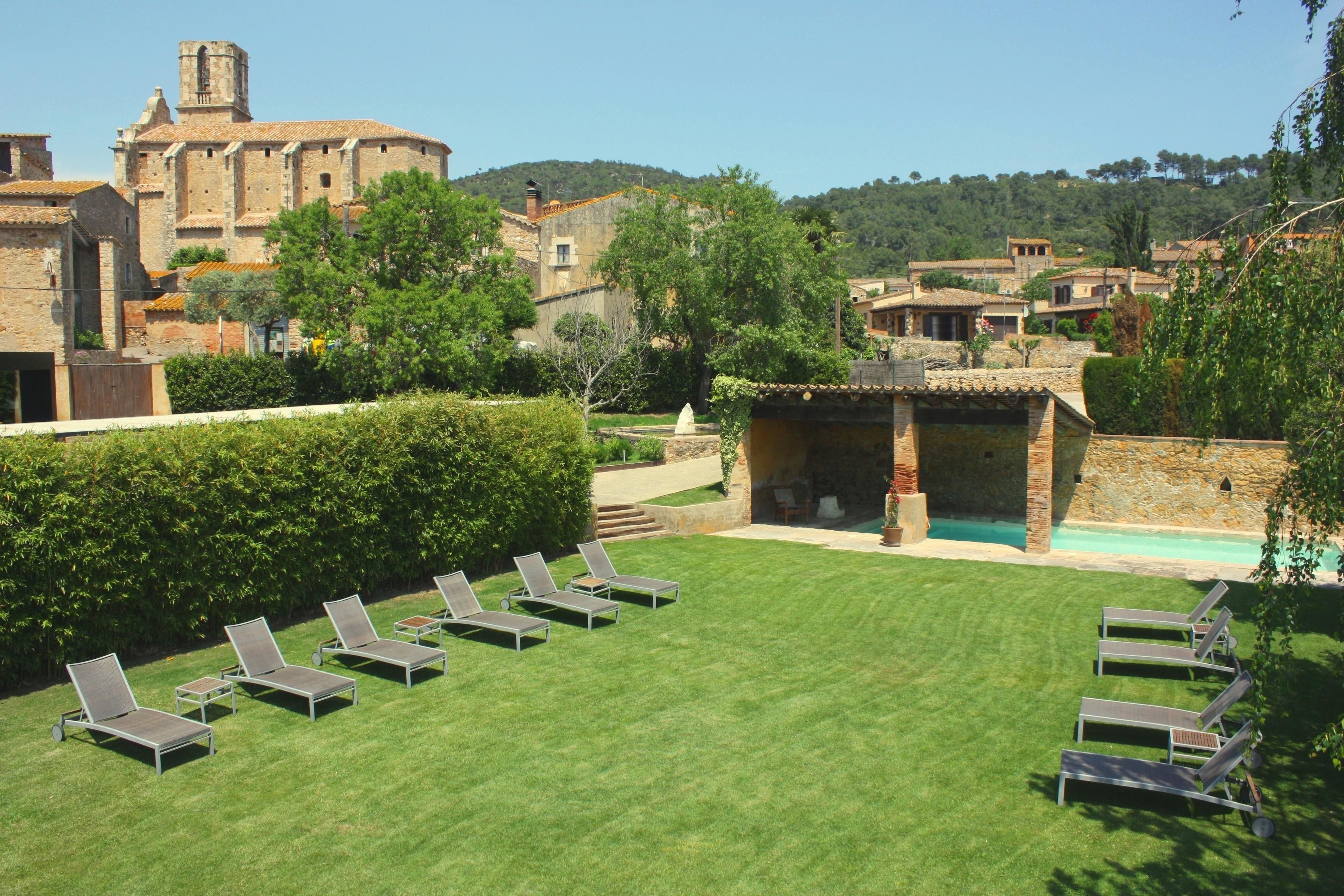 Un patio con piscina, sillas de descanso y un edificio histórico al fondo.