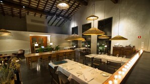 Un vaste espace dédié à la salle à manger, avec de longues tables disposées pour accueillir de nombreux convives, agrémenté de lampes en osier suspendues et d’un plafond haut avec des poutres apparentes.