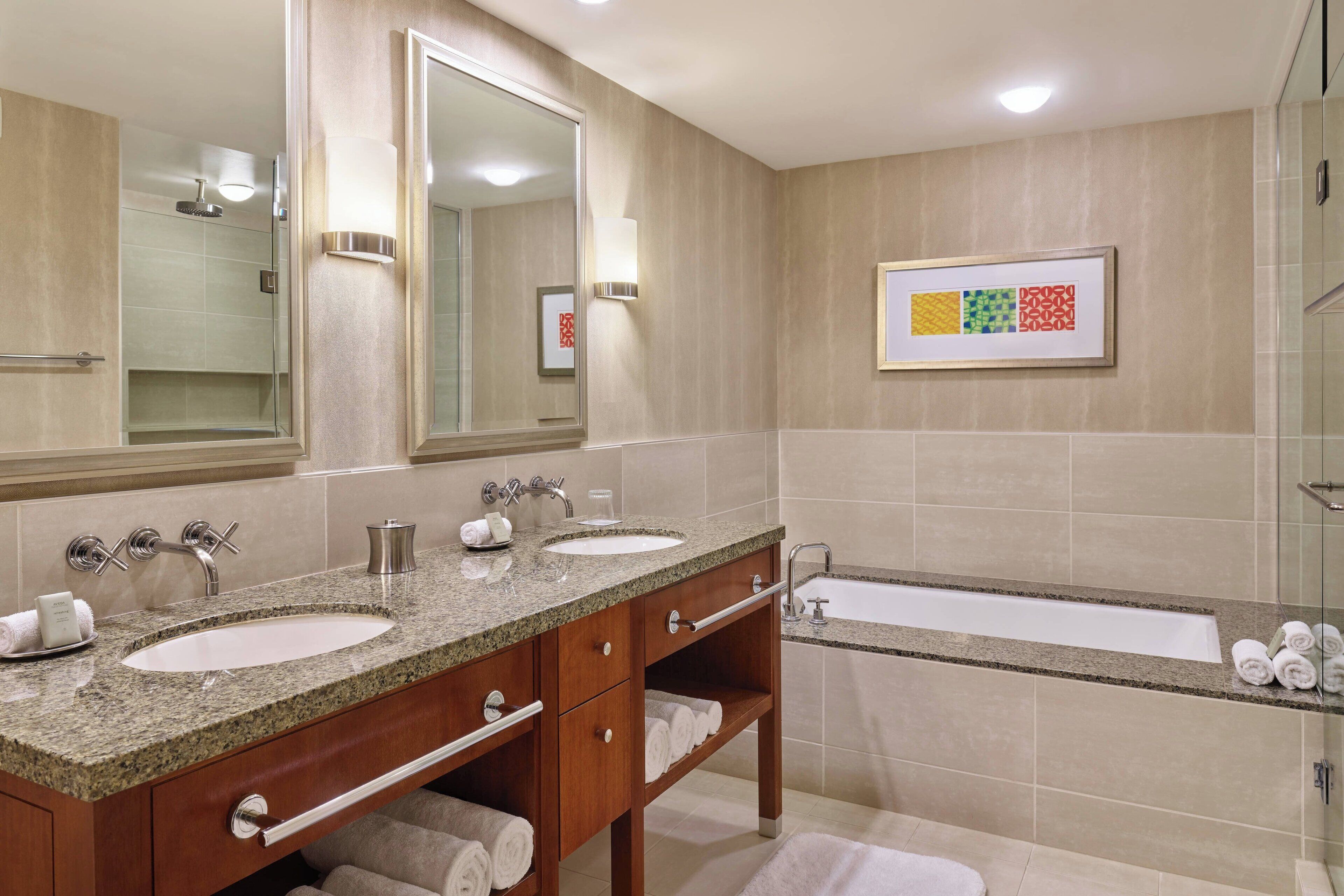 A modern bathroom with two sinks, a large mirror, and a bathtub.