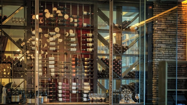 A restaurant interior with a long dining table, chairs, and a wine rack in the background.