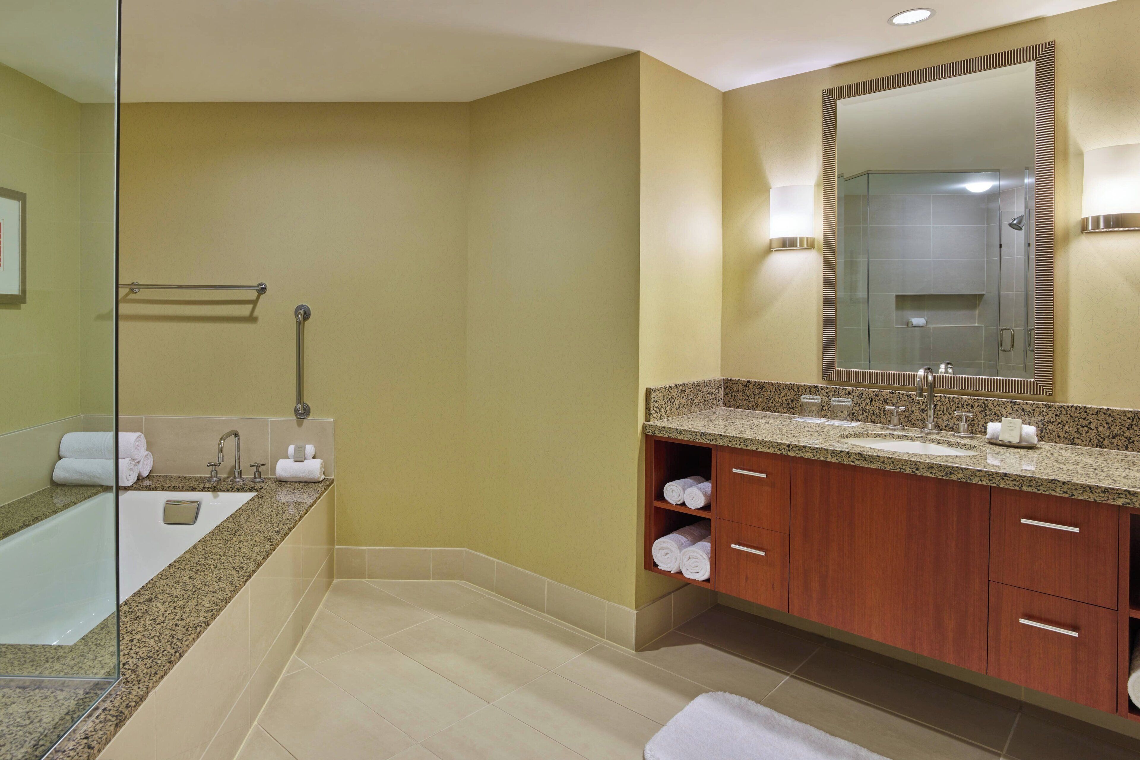 A modern bathroom with a large mirror, a bathtub, a sink, and wooden cabinets.