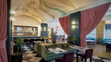 Un restaurante con suelo a cuadros, sofás verdes y cortinas rojas.