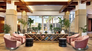 A lobby with a reception desk, two pink armchairs, a coffee table, and potted plants.