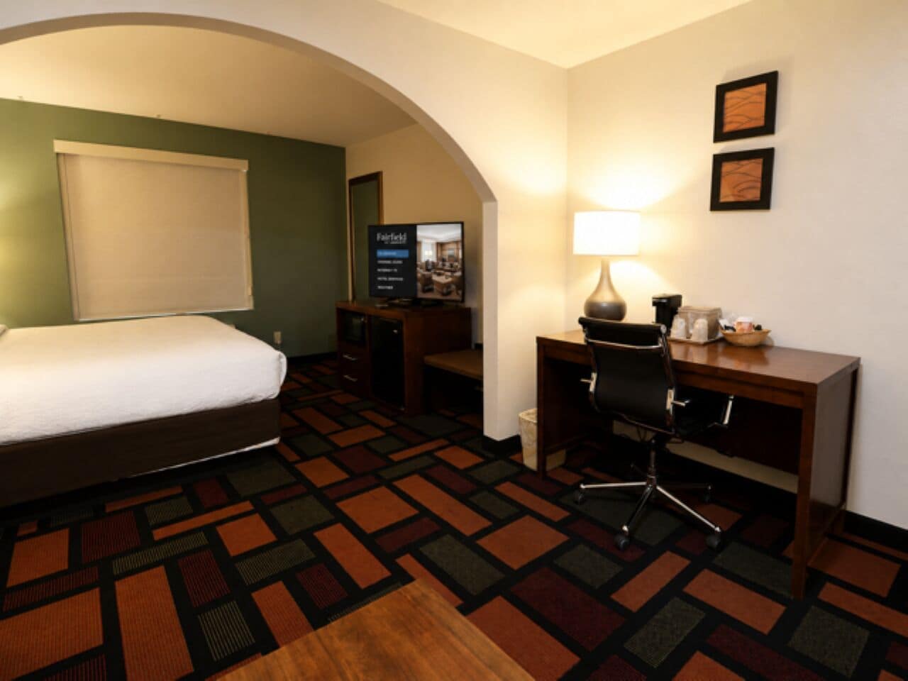 A hotel room with a bed, desk, chair, lamp, and a television.
