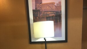 Habitación de hotel con dos sillones tapizados en rojo, una lámpara de pie y un cuadro con un puente en la pared.