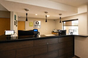 A hotel reception area with a digital check-in station, a sign indicating 'Quality by Choice Hotels,' and a welcome sign by the window.