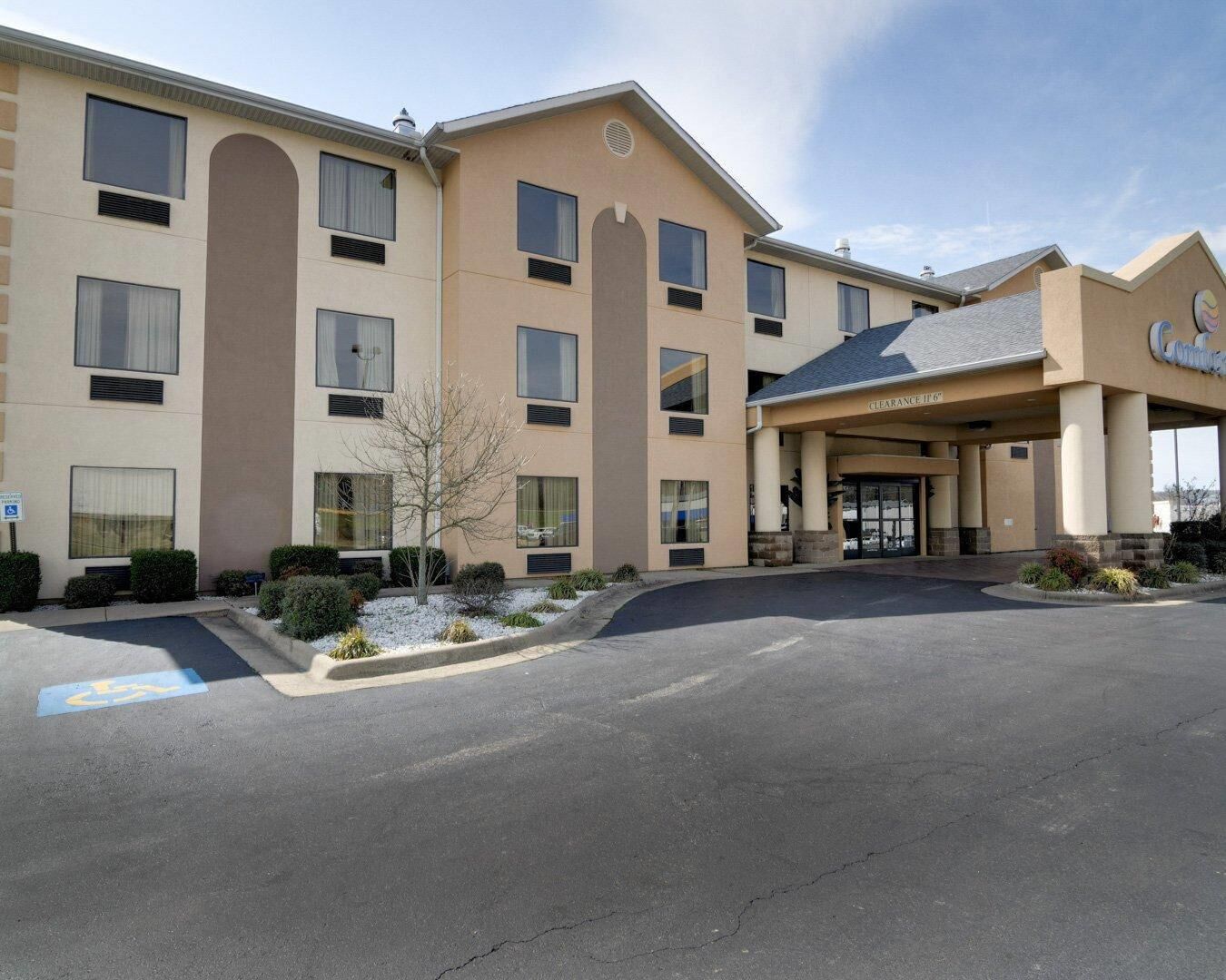 A multi-story hotel with a beige facade, a covered entrance, and a parking lot.