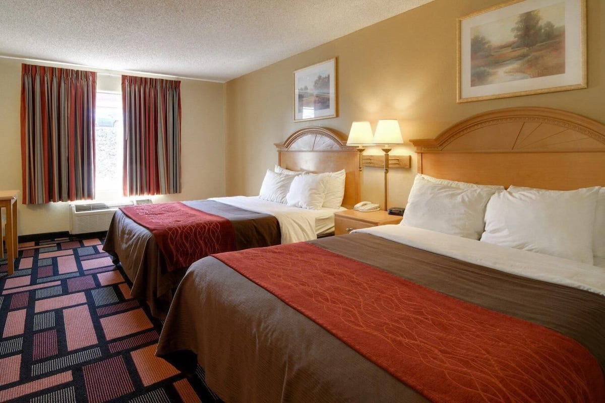 A hotel room with two beds, a desk, a chair, a lamp, and a painting on the wall.