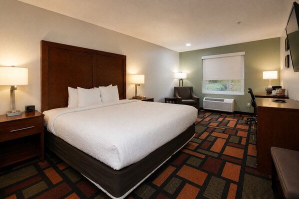 A hotel room with a large bed, two bedside tables with lamps, a chair, a desk with a lamp, and a window with a view.