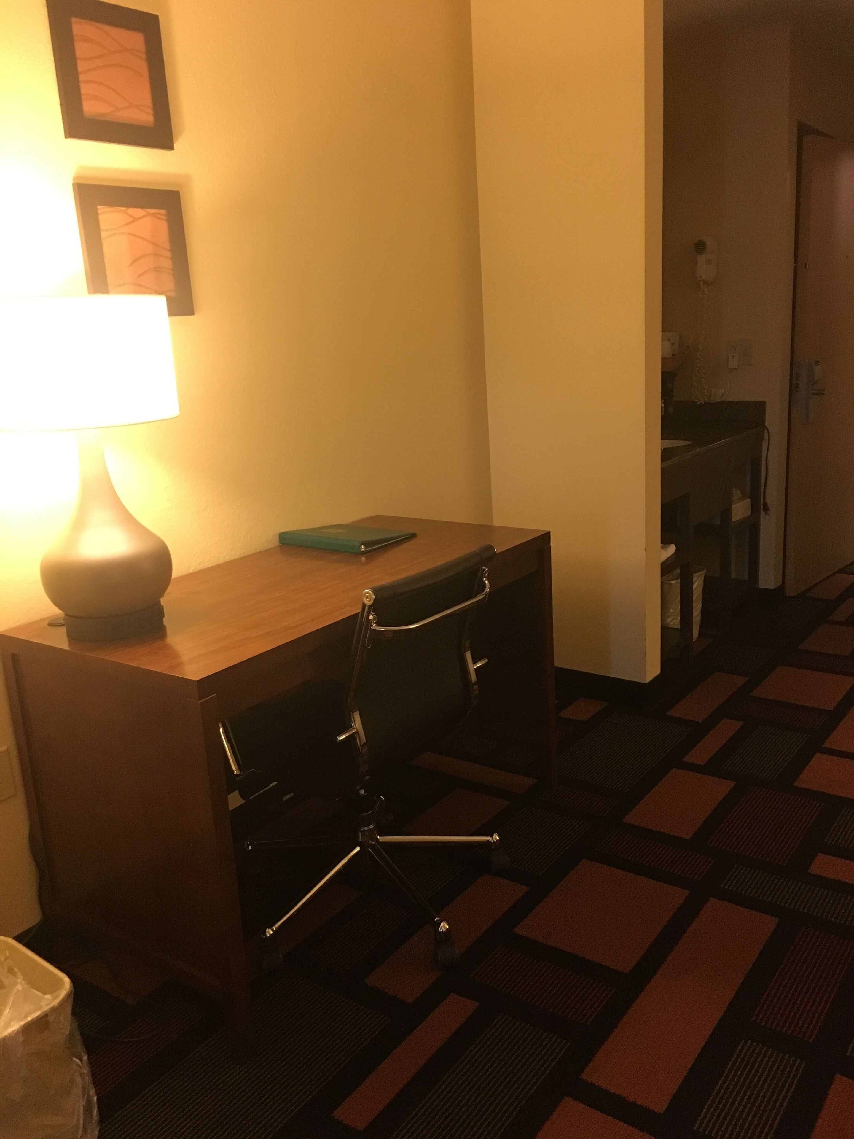 A hotel room with a desk, chair, lamp, and a small table with a book.