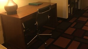 Habitación de hotel con escritorio, silla, lámpara y una mesita con un libro.