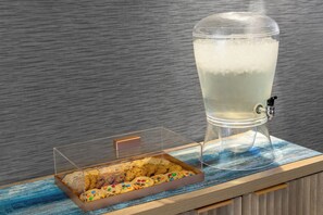 Vitrine de vidro transparente com biscoitos e um grande dispensador de água sobre um balcão de madeira.
