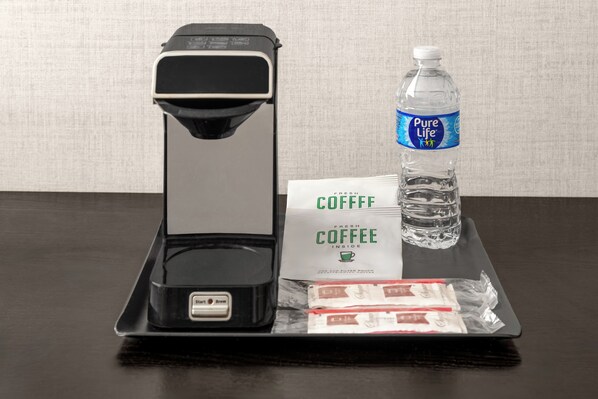 A coffee maker, a bottle of water, a coffee bag, and coffee pods on a tray.
