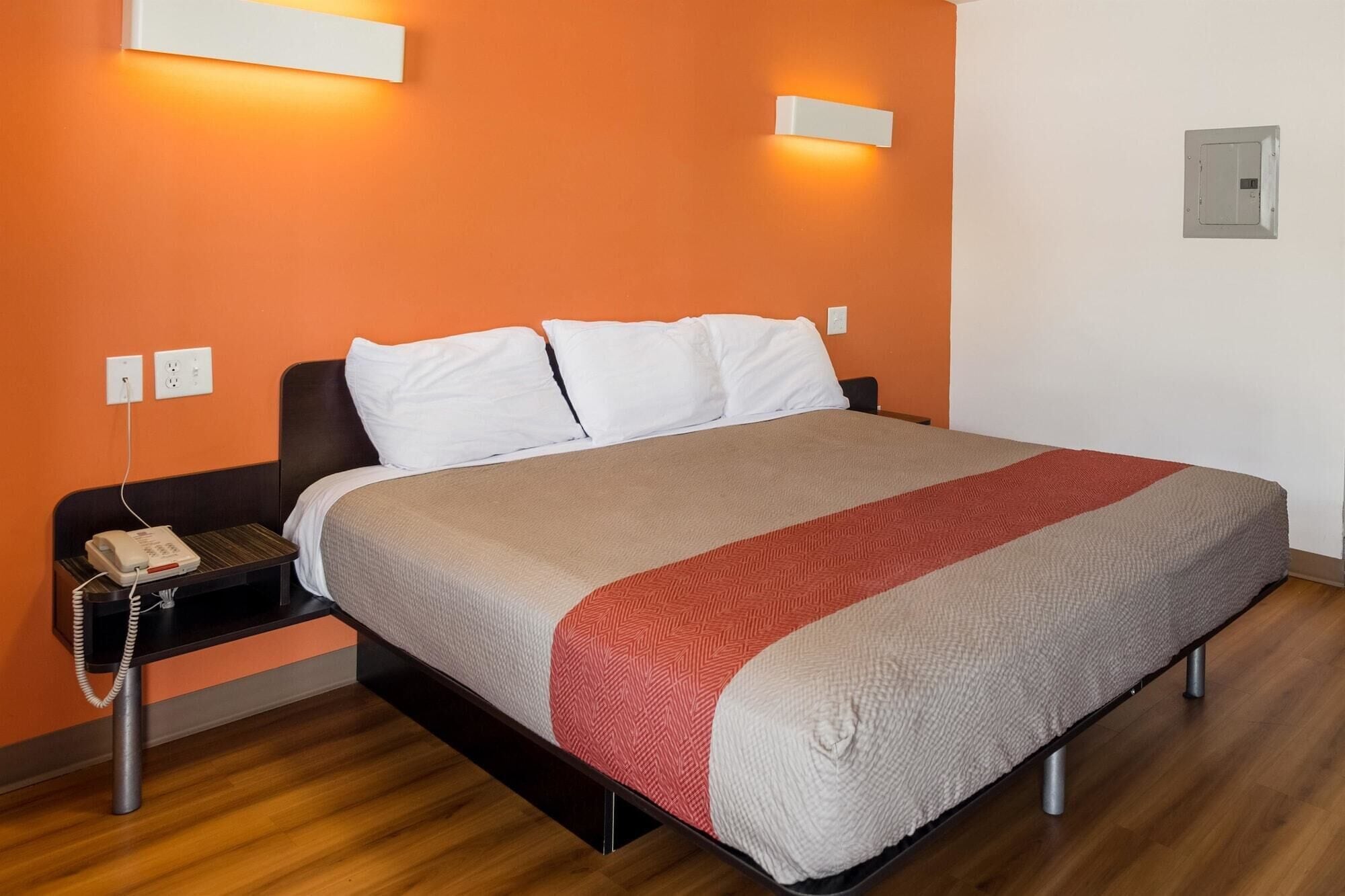A hotel room with a bed, a bedside table with a phone, and a wall socket.