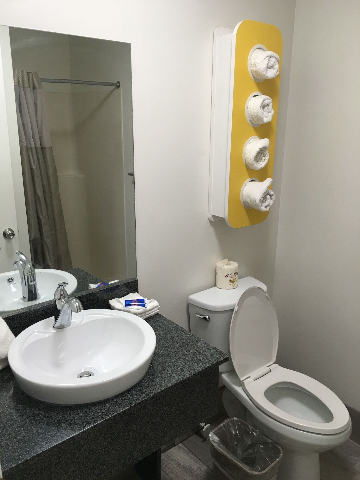 A bathroom with a sink, mirror, toilet, and towel dispenser.