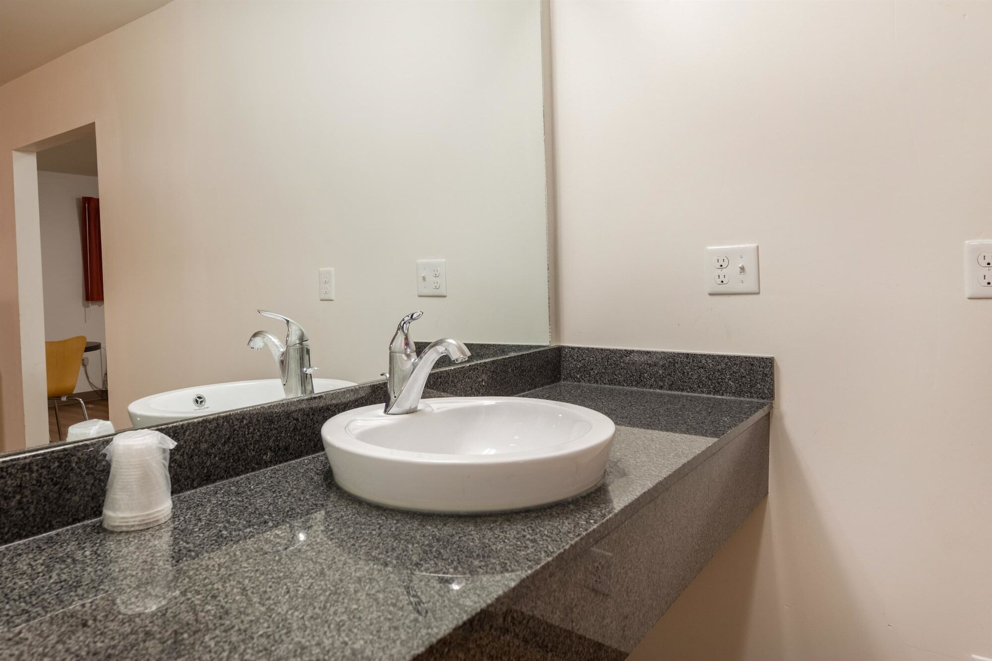 A bathroom with a white sink, two faucets, a mirror, and a granite countertop.