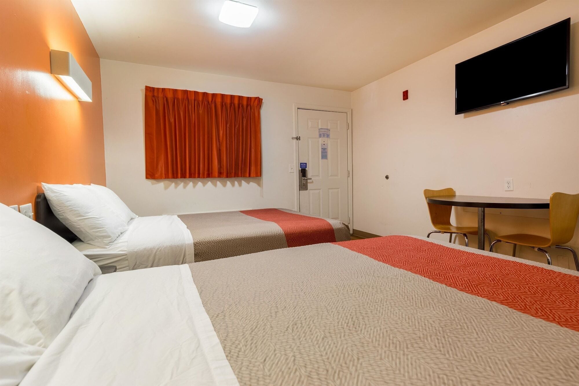 Une chambre d’hôtel avec deux lits, un bureau, une chaise, une télévision et une porte.
