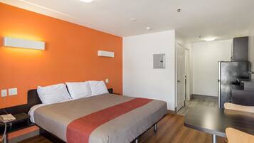 A hotel room with a bed, bedside table, and a kitchenette area.