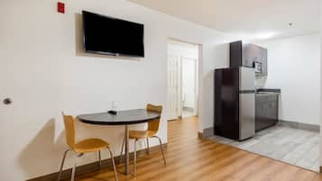 Eine moderne Küche mit integriertem Kühlschrank, einer Mikrowelle und einem flachbildfernseher an der Wand. Es gibt einen Essbereich mit einem runden Tisch und zwei Stühlen.