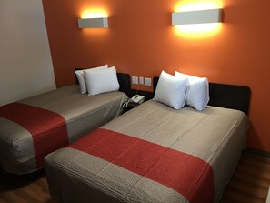 Habitación de hotel con dos camas, cada una con colcha roja y beige, almohadas blancas y teléfono junto a la cama.