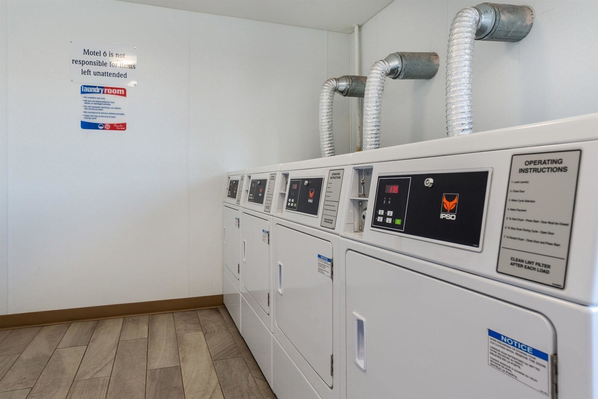 Een wasserette met meerdere wasmachines en drogers, ventilatiekanalen aan de muur, en bedieningsinstructies op de machines.