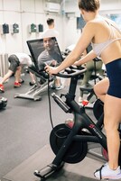 Egy edzőterem, amelyben állókerékpárok, futópadok találhatók, és egy személy éppen egy fitneszkerékpáron edz.