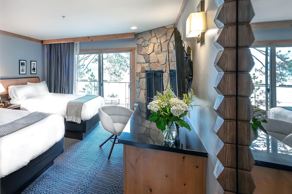 A hotel room with two beds, a stone fireplace, a large window, and a view of the outdoors.