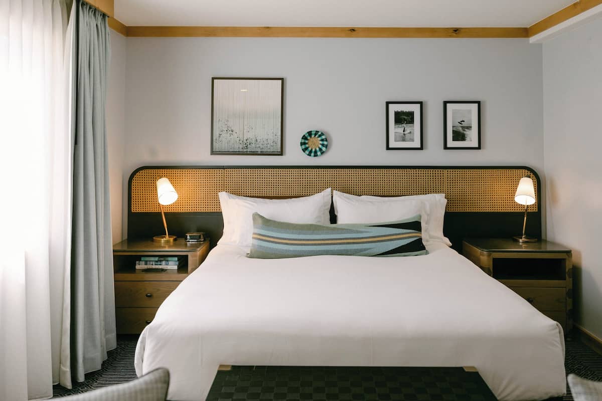A hotel room with a large bed, two bedside tables with lamps, a headboard with a woven design, and a wall with framed pictures and a decorative plate.