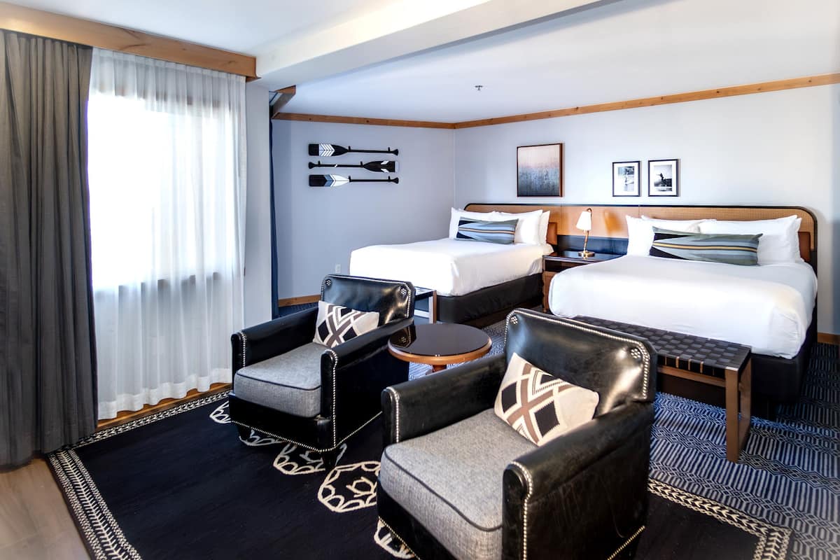 A hotel room with two beds, a sofa, a chair, a small table, and a window with curtains.