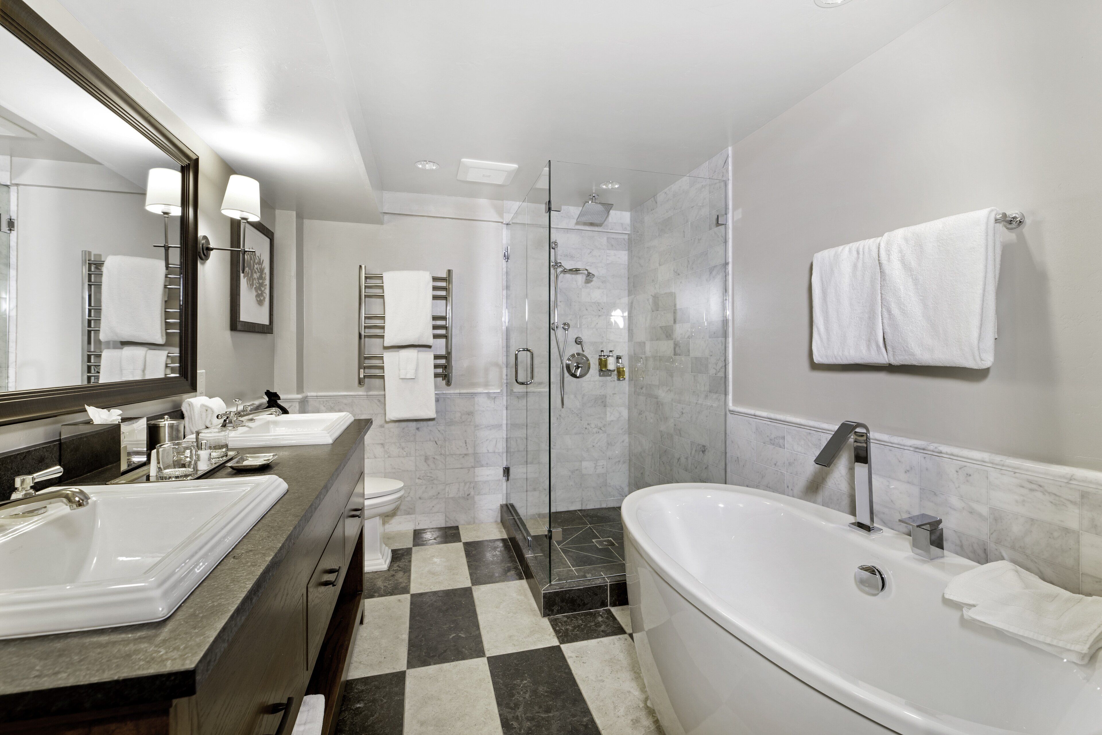 A modern bathroom with two sinks, a large bathtub, a glass-enclosed shower, and a checkered floor.