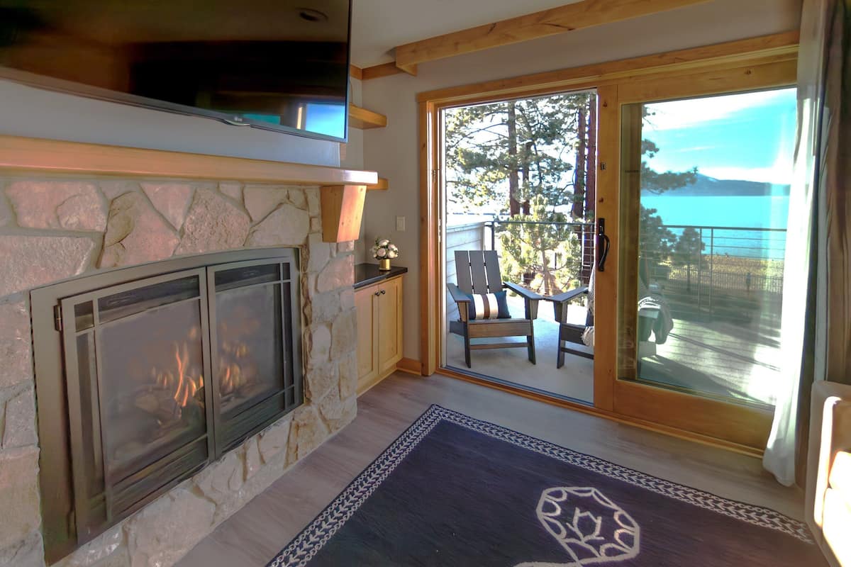 A stone fireplace with a glass screen, a wooden ceiling, and a view of a balcony with outdoor furniture.