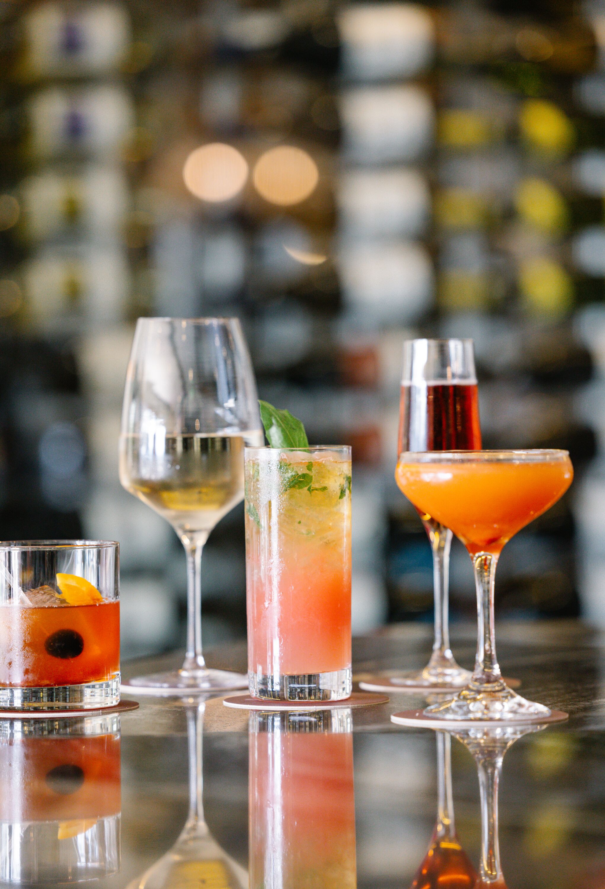Four different types of drinks in various glassware on a bar counter.