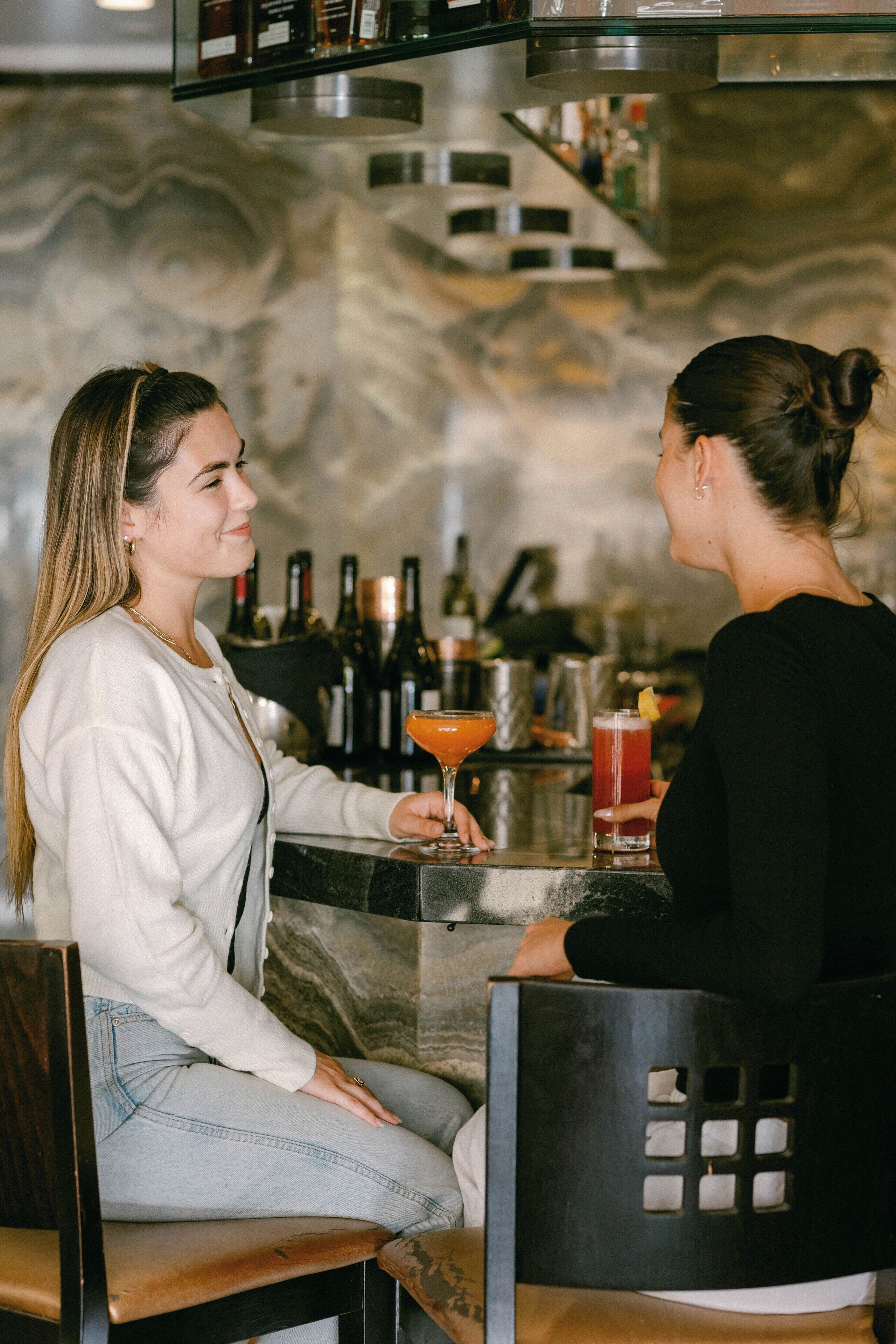 Dos personas sentadas en una barra con una pared de mármol al fondo.