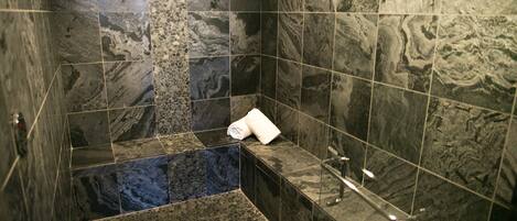 A bathroom with a marble floor and walls, a bathtub, and a shower area.