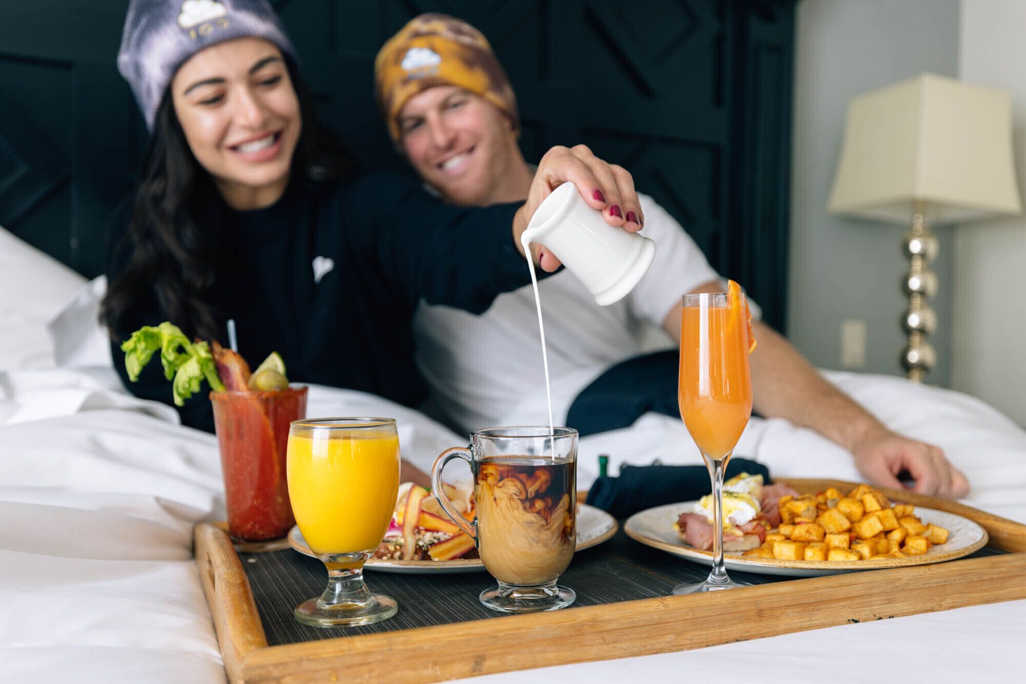 A breakfast tray with orange juice, coffee, and a plate of hash browns on a bed.